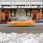 The Plaza Hotel exterior in New York City with a yellow taxi passing by