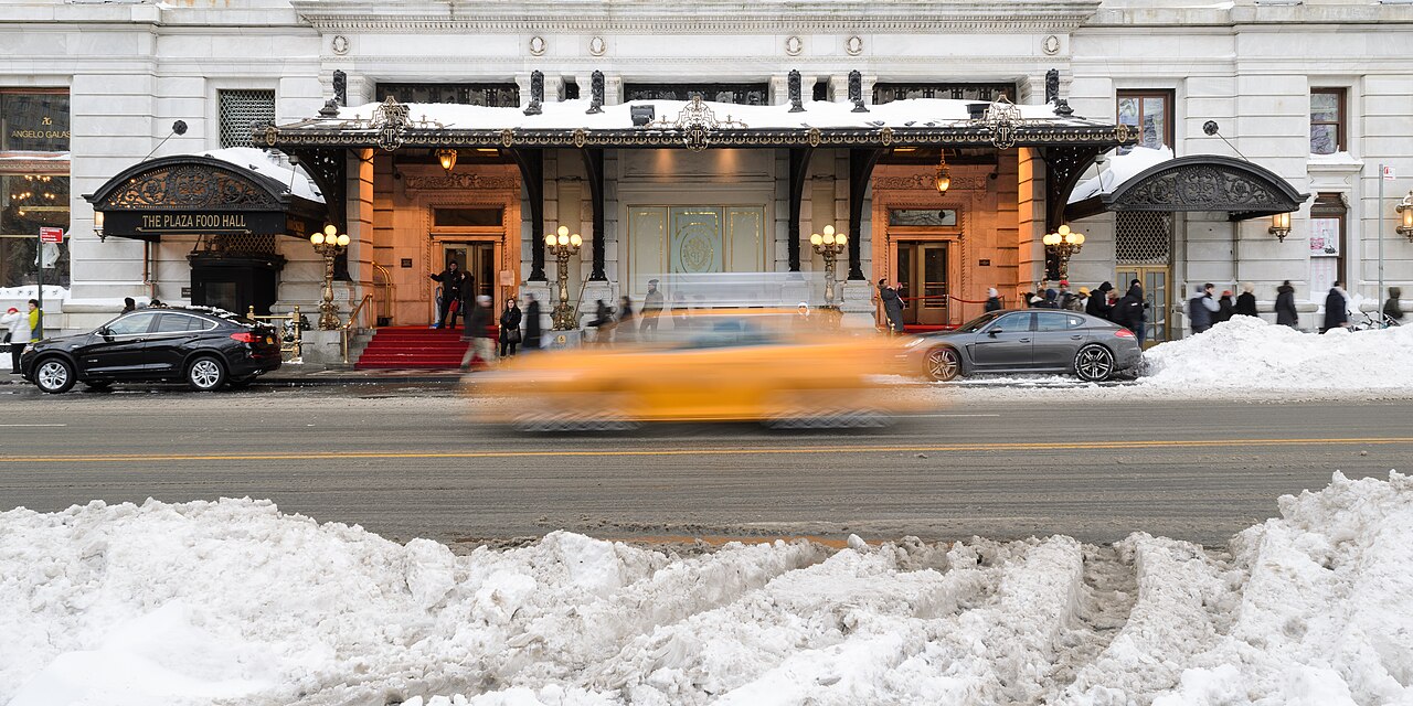 The Plaza Hotel exterior in New York City with a yellow taxi passing by